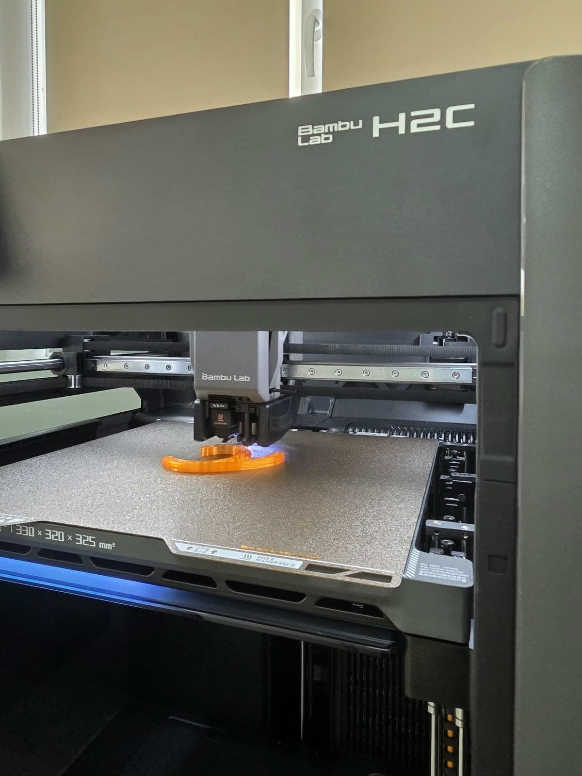 Fotografie reală: Bambu Lab H2C în lucru la CHT-TECH, printând o piesă portocalie
